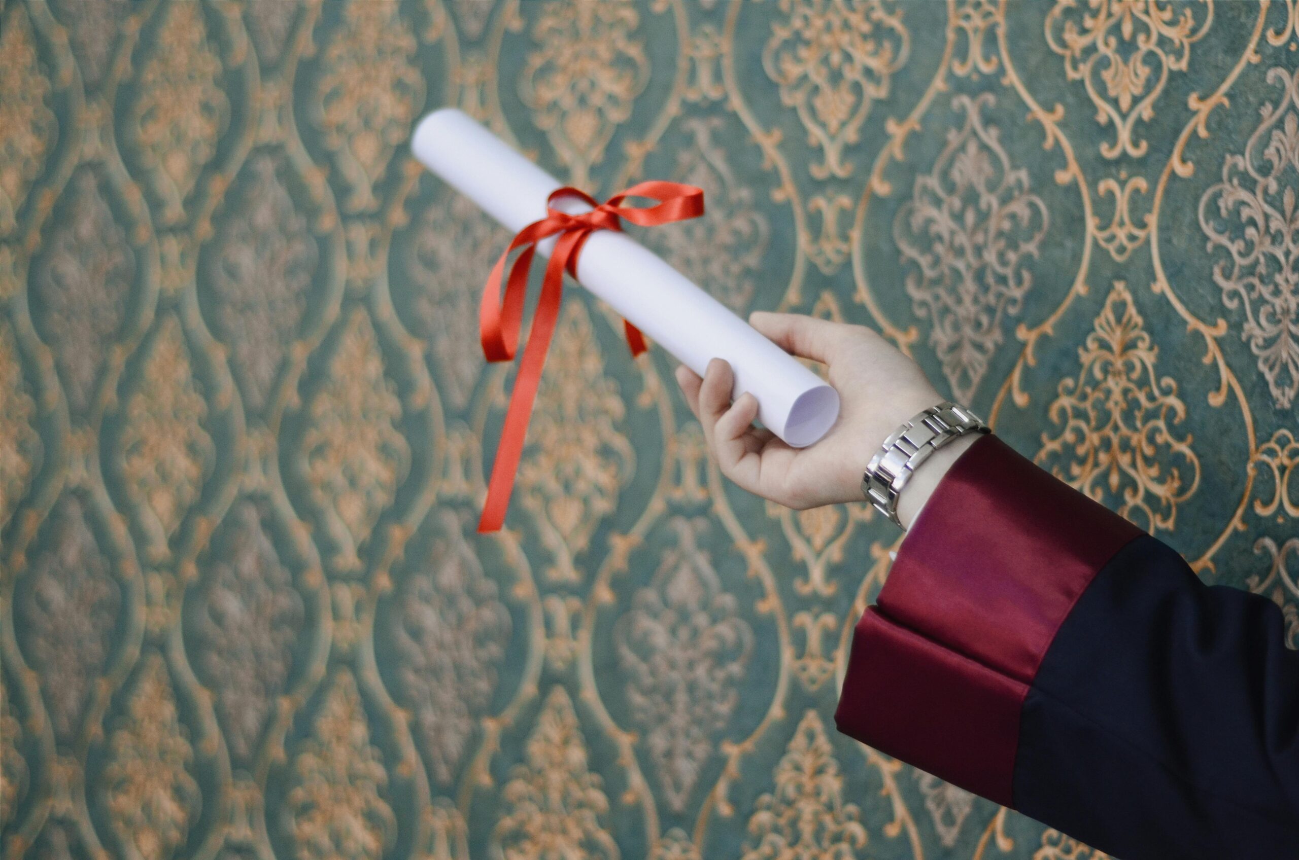A graduate's hand holding a diploma with red ribbon, symbolizing achievement.